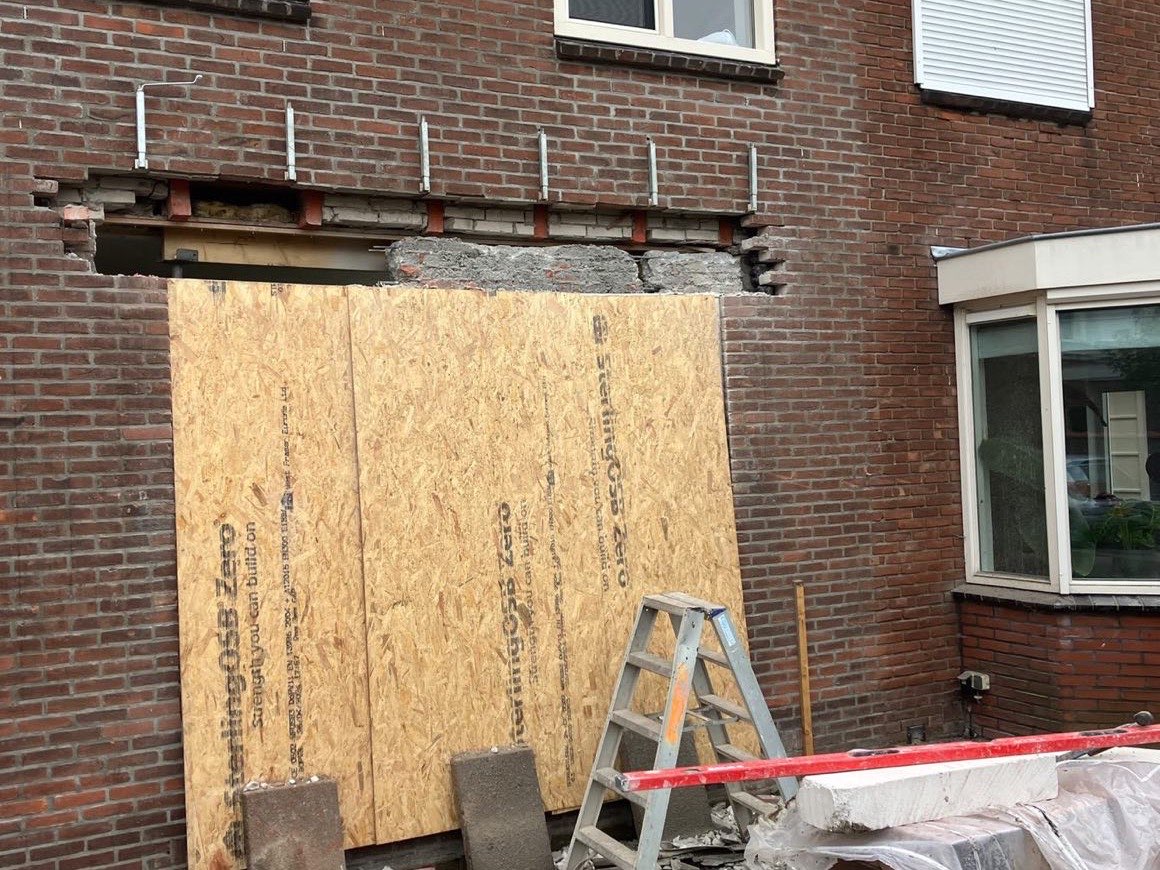 Gevel met een grote doorbraak, dichtgezet met een houten plaat en ondersteund met stempels