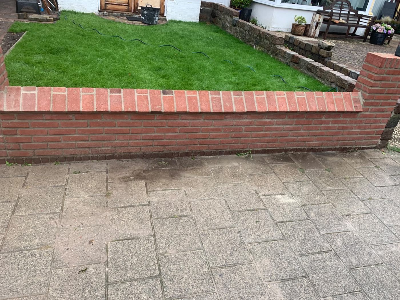 Nieuw gemetseld muurtje van rode baksteen rond een voortuin met gras